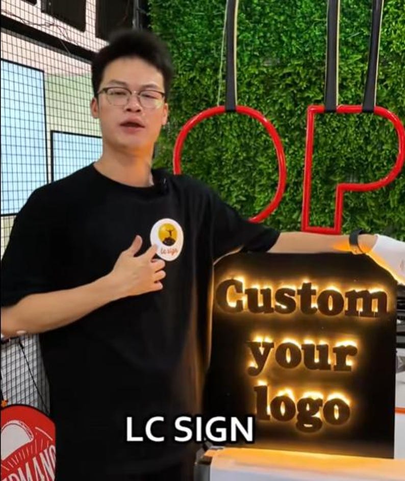 May include: A rectangular black sign featuring the illuminated text "Custom your logo" in a bold, serif font. The sign is positioned below a red circular frame and is accompanied by the text "LC SIGN" displayed at the bottom of the image.