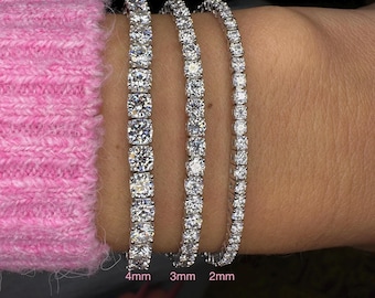 May include: Three diamond tennis bracelets in varying sizes: 4mm, 3mm, and 2mm. The bracelets are displayed on a wrist, showcasing the different stone sizes and overall design. The bracelets are set in a silver metal.