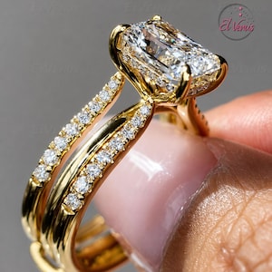 May include: A gold ring featuring a large rectangular radiant-cut center stone held by four prongs. The band is split into two rows, each encrusted with small round pavé-set diamonds. The metal has a polished finish and the logo El Venus is visible.
