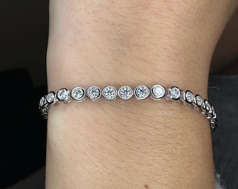 May include: A silver bracelet with round, clear gemstones set in individual bezels. The bracelet is shown on a person's wrist, with the gemstones reflecting light. The bracelet is a delicate piece of jewelry.