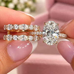 May include: A gold engagement ring set featuring a large oval-cut center stone with a halo of smaller round stones. The set includes two matching bands adorned with alternating oval and round-cut stones, all set in a polished gold metal band.