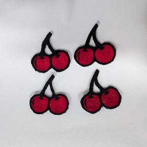 May include: Four embroidered patches of red cherries, each pair with a black stem and outline. The patches are set against a white backdrop, highlighting the bright red fruit.
