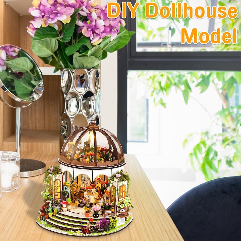 May include: A DIY dollhouse model with a domed roof, featuring miniature plants and furniture. The model is surrounded by greenery and flowers, with the text "DIY Dollhouse Model" in the upper right corner. The dollhouse is on a wooden surface.