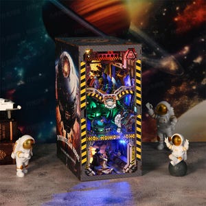 Puede incluir: Un diorama detallado e iluminado de una estación espacial con astronautas y una nave espacial. El diorama está alojado en una caja rectangular con un interior detallado, con varios niveles y efectos de iluminación. Figuras de astronautas están colocadas alrededor.