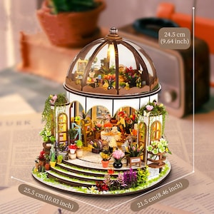 May include: Miniature wooden greenhouse model with a glass dome, featuring detailed interior and exterior floral arrangements. Dimensions: 10.03 inches (25.5 cm) wide, 8.46 inches (21.5 cm) deep, and 9.64 inches (24.5 cm) high. Includes the text "FURK".