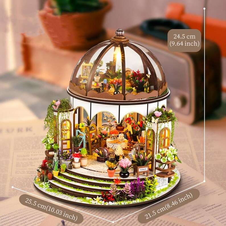 May include: Miniature wooden greenhouse model with a glass dome, featuring detailed interior and exterior floral arrangements. Dimensions: 10.03 inches (25.5 cm) wide, 8.46 inches (21.5 cm) deep, and 9.64 inches (24.5 cm) high. Includes the text "FURK".