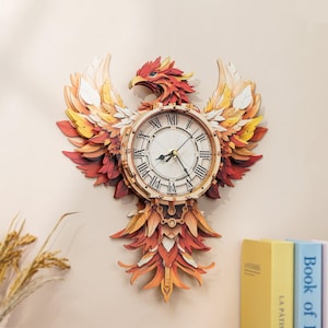 May include: A wall clock featuring a layered wooden phoenix design with outstretched wings. The clock face is circular with black Roman numerals and thin black hands. The phoenix is coloured in shades of red, orange, yellow, and cream, creating a dimensional effect with its detailed feather cutouts and prominent head.