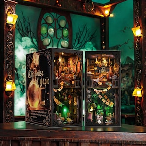 Könnte beinhalten: Zwei beleuchtete Miniatur-Diorama-Boxen mit aufwendigen Innendetails, die einen magischen Laden darstellen. Die linke Box zeigt den Text "The House of Magic". Die Boxen sind vor einem dunkelgrünen Hintergrund mit dekorativer Beleuchtung platziert.