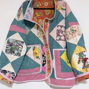 May include: A quilted jacket with a patchwork design. The jacket features a teal background with floral and geometric patterns, accented by pink and yellow details. The interior lining is a vibrant floral print.