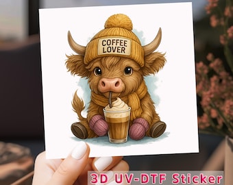 Puede incluir: Una ilustración de dibujos animados de una vaca de las Tierras Altas con un gorro amarillo con el texto "Coffee Lover" y bebiendo una bebida de café con crema batida.