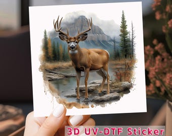 May include: A 3D UV-DTF sticker featuring a watercolor illustration of a white-tailed deer standing in a forest stream. The deer has large antlers and is surrounded by trees and mountains.
