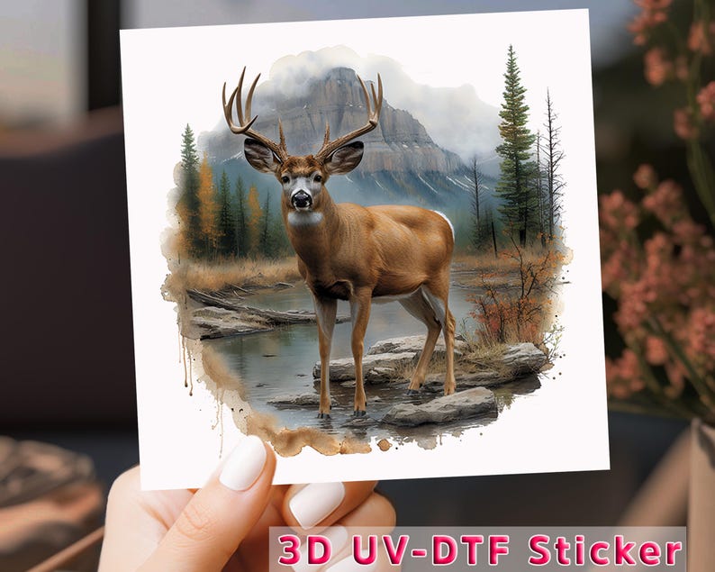 May include: A 3D UV-DTF sticker featuring a watercolor illustration of a white-tailed deer standing in a forest stream. The deer has large antlers and is surrounded by trees and mountains.