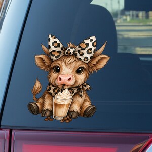 May include: A brown cartoon cow sticker with a large bow and scarf, both with a leopard print design. The cow is drinking a coffee drink with whipped cream. Coffee beans are scattered around the drink.