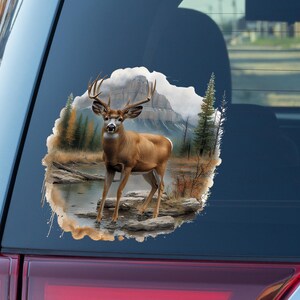 May include: A brown and white deer with large antlers stands in a forest setting. The deer is looking directly at the viewer. The background is a watercolor-style painting of trees, mountains, and a river.