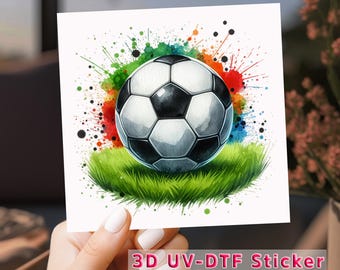 May include: A soccer ball illustration with a black and white design, set on green grass, and surrounded by colorful paint splatters. The image is a sticker with the text "3D UV-DTF Sticker".