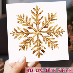 May include: A gold glitter snowflake sticker on a white background. The snowflake has six points with detailed edges. The sticker has the text "3D UV-DTF Sticker" at the bottom.
