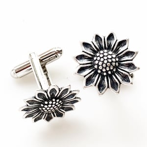 Puede incluir: Un par de gemelos de plata con diseño de girasol. Los gemelos están detallados con un centro texturizado y pétalos.