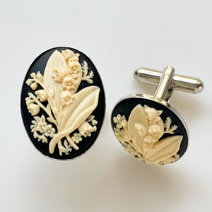 Puede incluir: Un par de gemelos de plata con esmalte negro y un camafeo blanco de flores de lirio de los valles.