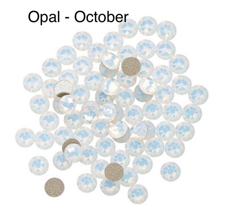 May include: A pile of white opal rhinestones, also known as October birthstones. The rhinestones are scattered on a white background.