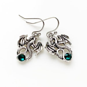 May include: Silver dragon earrings with green gemstone accents. The dragon is curled around the gemstone.