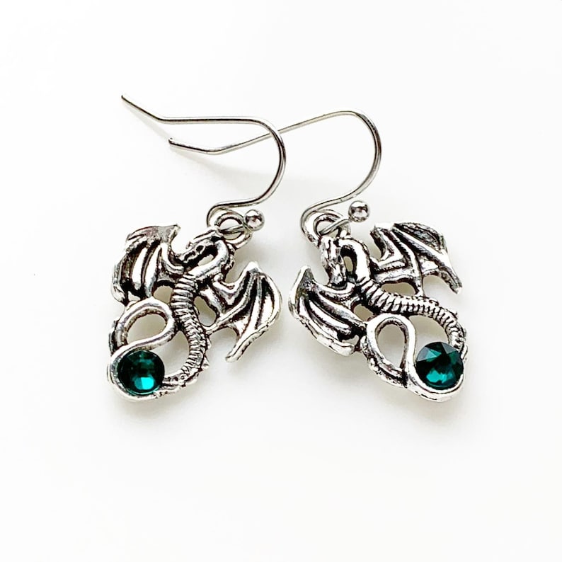 May include: Silver dragon earrings with green gemstone accents. The dragon is curled around the gemstone.