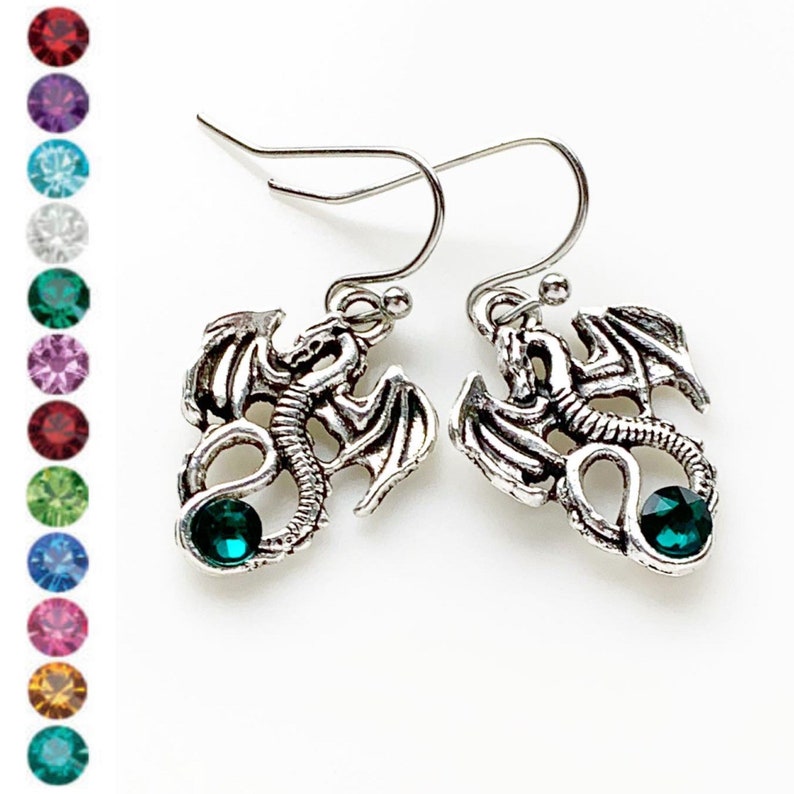 May include: Silver dragon earrings with green crystal accents. The dragon is in a curled position with its wings spread out.