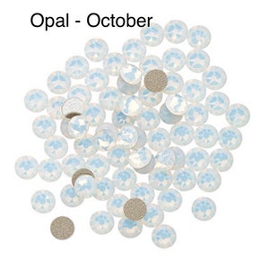 May include: A pile of white opal rhinestones, also known as October birthstones. The rhinestones are scattered on a white background.