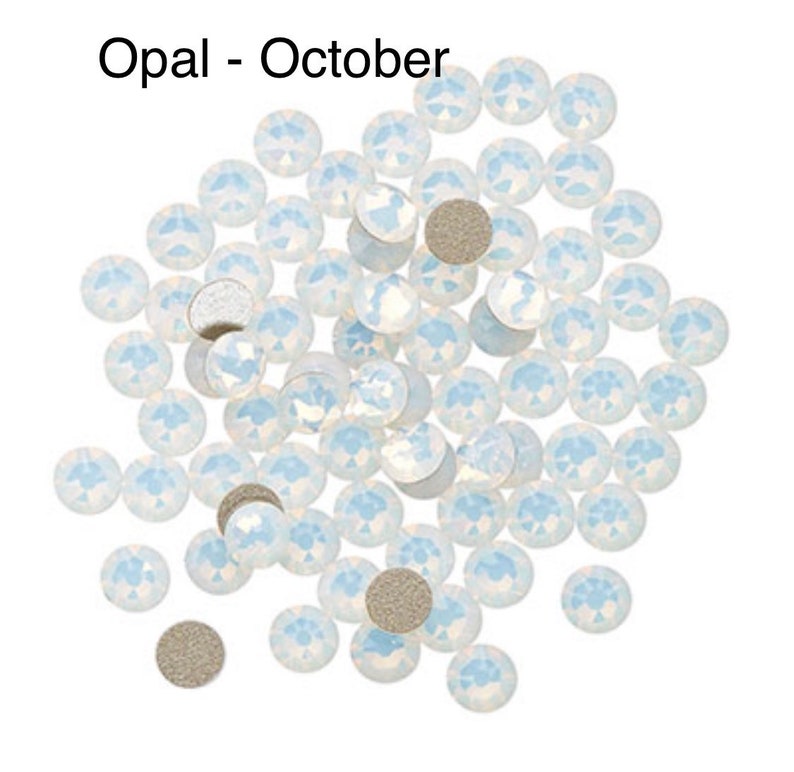 May include: A pile of white opal rhinestones, also known as October birthstones. The rhinestones are scattered on a white background.