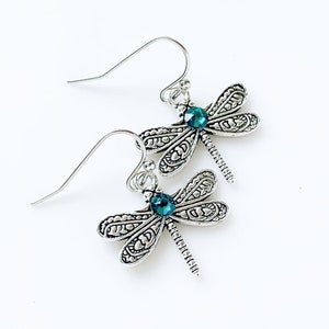 May include: Silver dragonfly earrings with teal blue crystal accents. The earrings have a detailed design and dangle from silver hooks.