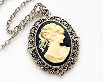 Puede incluir: Un collar de cadena de plata con un colgante de camafeo. El camafeo presenta un perfil blanco de una mujer sobre un fondo negro y un marco de plata adornado.