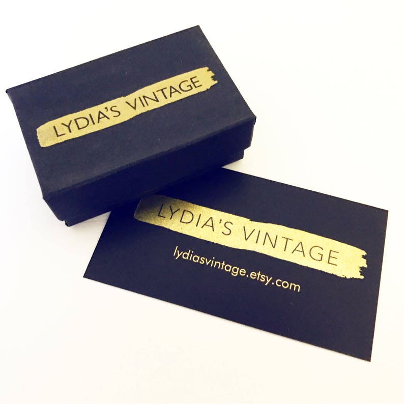 K&ouml;nnte beinhalten: Schwarze Box mit goldener Aufschrift "LYDIA'S VINTAGE". Eine schwarze Karte mit goldener Aufschrift "LYDIA'S VINTAGE" und der Website "lydiasvintage.etsy.com".
