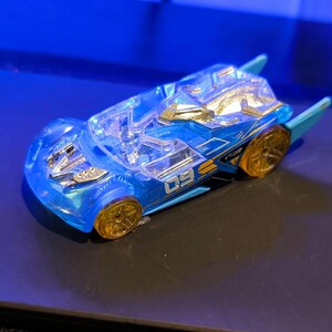 May include: A blue and gold toy car with clear windows and gold wheels. The car has a futuristic design with wing-like extensions and the number "09" printed on the side. The toy car is a die-cast model.