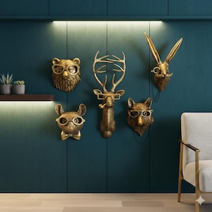 May include: A set of gold-toned animal head wall sculptures, featuring a bear, deer, rabbit, fox, and mouse, each sporting spectacles. The deer holds a pipe. They are mounted on a dark teal wall, offering a quirky and decorative feature.