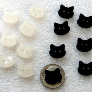 May include: A collection of cat-shaped buttons in two colors: off-white and black. The buttons are small, with two holes for sewing. A dime is included for size comparison. The buttons are arranged on a white, textured surface.