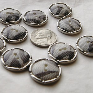 May include: A collection of decorative buttons with a snake skin pattern in shades of gray and white. Each button has a silver-colored rim and a two-hole design. A U.S. nickel is included for size comparison.