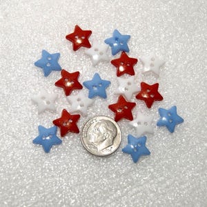 May include: A collection of star-shaped buttons in red, white, and blue. The buttons have two holes for sewing. A U.S. dime is included for size comparison. The buttons are likely for crafts or sewing projects.
