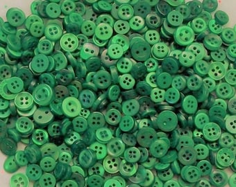May include: A large pile of green plastic buttons. The buttons are all the same size and shape, and they have four holes each.