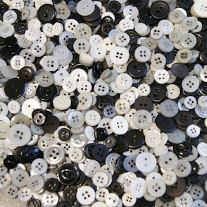 May include: A collection of various sizes of buttons in shades of black, white, and gray. The buttons have two or four holes and are scattered across the image. The buttons are made of plastic and are suitable for sewing and crafts.