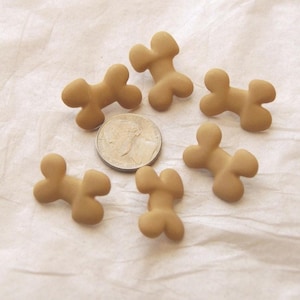 May include: Five tan, bone-shaped objects arranged in a circle around a silver United States dime. Each bone-shaped piece has a smooth, matte finish with rounded edges and a central indentation, providing a clear scale reference for their size.