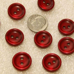 Peut inclure: Plusieurs boutons rouges à deux trous. Les boutons sont d'un rouge profond et translucide avec une finition brillante. Une pièce de monnaie est incluse pour la comparaison des tailles. Idéal pour la couture.