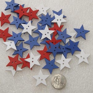 May include: A collection of wooden star-shaped buttons in red, white, and blue. The buttons have two holes each and are approximately 1 inch in diameter.