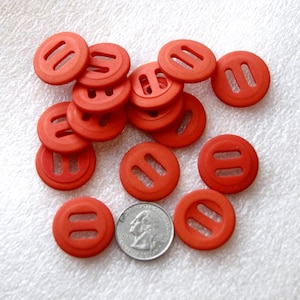 May include: A collection of round, red buttons with two parallel slots and a central hole. A U.S. quarter is included for size comparison. The buttons are scattered on a white surface.