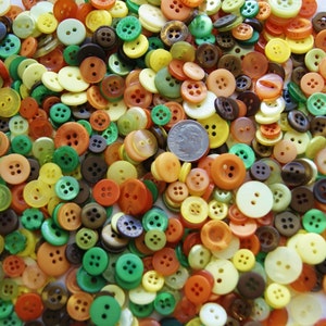 May include: A large collection of colorful buttons in various sizes and shapes. The buttons are mostly round, but there are also some square and oval buttons. The colors include green, yellow, orange, brown, and white.