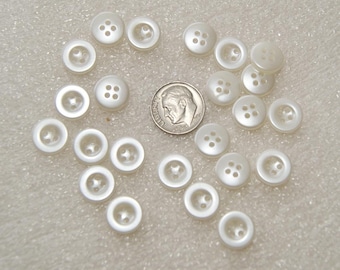 Könnte beinhalten: Eine Sammlung von 20 weißen Plastikknöpfen mit jeweils vier Löchern. Die Knöpfe sind in einem Kreis um eine US-amerikanische 50-Cent-Münze angeordnet.
