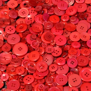 Peut inclure: Une grande collection de boutons en plastique rouge de différentes tailles et formes.