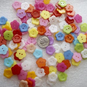 May include: A collection of colorful flower-shaped buttons in various shades, including pink, yellow, blue, orange, and green. Each button has two or four holes for sewing. A US dime is included for size reference.