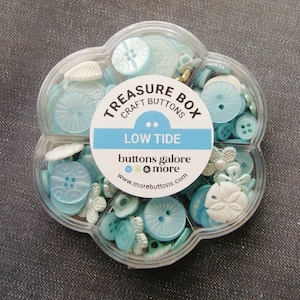 May include: A clear plastic flower-shaped container filled with assorted blue and white buttons. The container has a label that reads "Treasure Box Craft Buttons Low Tide buttons galore & more www.morebuttons.com"