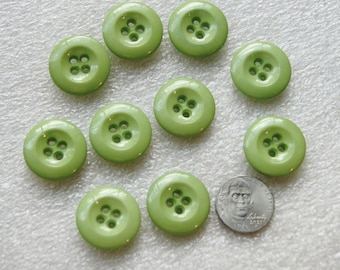 May include: A collection of ten light green, round buttons with four holes each. The buttons are arranged on a light-colored surface, with a silver coin for size comparison.