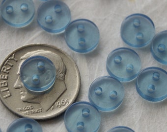 May include: A close-up of a pile of light blue plastic buttons with two holes each. The buttons are about the size of a dime.