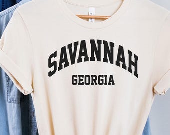 Puede incluir: Una camiseta de color crema con texto negro que dice "SAVANNAH GEORGIA" en una fuente arqueada.